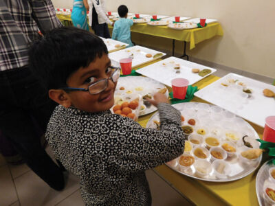 A young devotee eagerly helps with setting up the plates. page-chhapanbhog-02